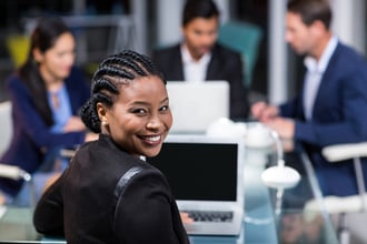 Portrait of businesswoman smiling at camera while colleagues interacting in the background
